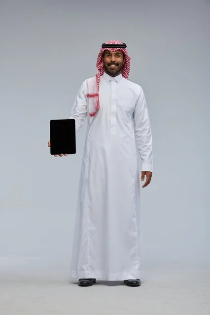 رجل سعودي مبتسم يمسك جهاز لوحي في استوديو تصوير