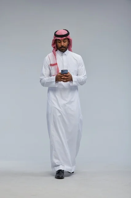 رجل سعودي بالزي التقليدي يستخدم هاتف ذكي في الاستوديو