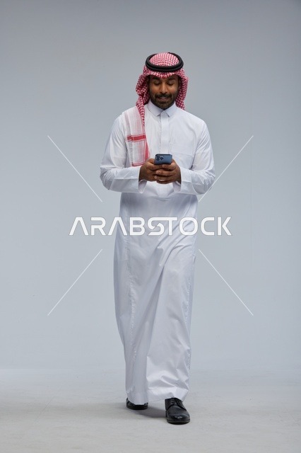 رجل سعودي بالزي التقليدي يستخدم الهاتف الذكي