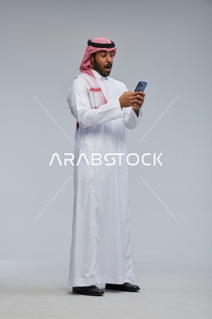 رجل سعودي مندهش يستخدم الهاتف الذكي بالزي التقليدي