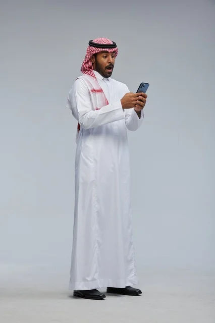 رجل سعودي مندهش يستخدم الهاتف الذكي بالزي التقليدي