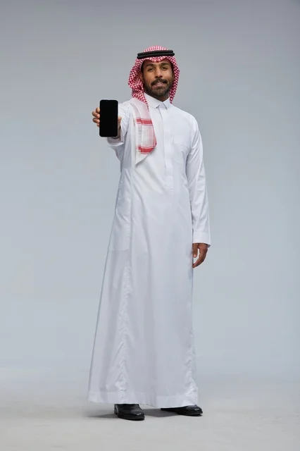 رجل سعودي يحمل هاتفاً ذكياً بالزي التقليدي