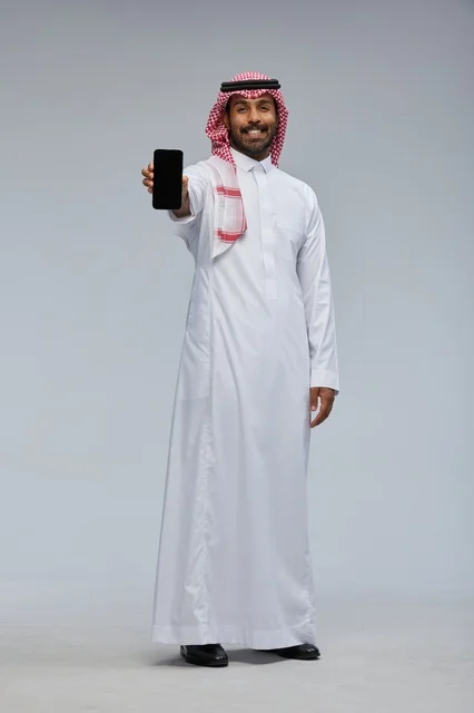رجل سعودي يرتدي الزي التقليدي يحمل هاتفاً ذكياً