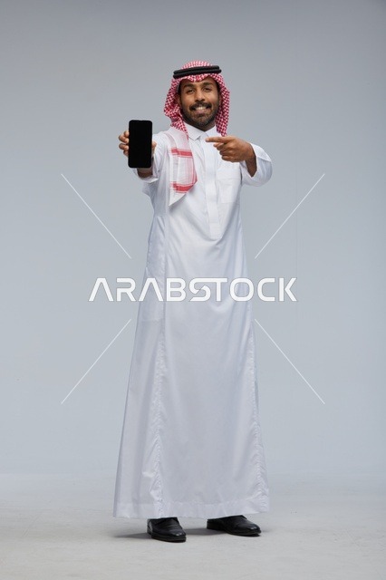 رجل سعودي يمسك هاتفاً ذكياً ويشير إلى الشاشة