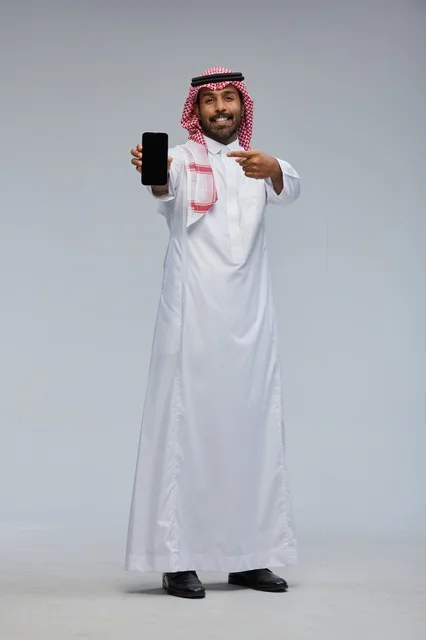 رجل سعودي يمسك هاتفاً ذكياً ويشير إلى الشاشة