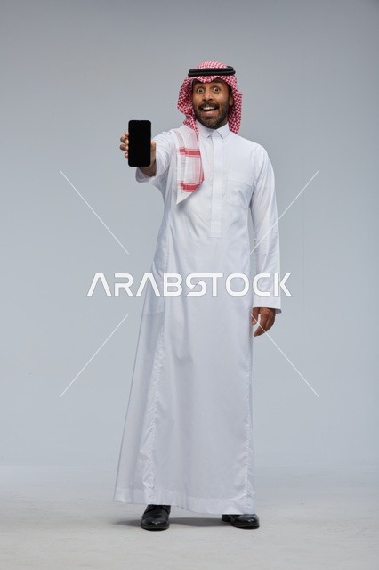 رجل سعودي يحمل هاتفاً ذكياً بتعبير وجه مندهش
