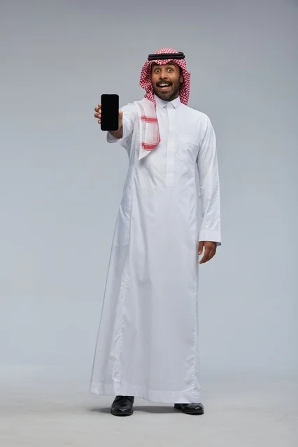 رجل سعودي يحمل هاتفاً ذكياً بتعبير وجه مندهش