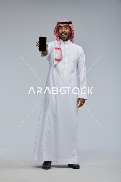رجل سعودي يحمل هاتف ذكي بتعبير وجه مندهش
