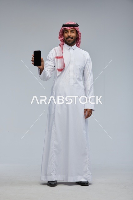 رجل سعودي يحمل هاتفاً ذكياً بشاشة فارغة في استوديو
