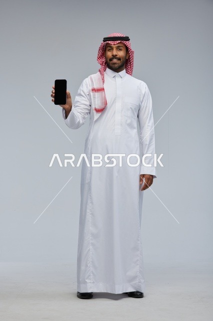 رجل سعودي يحمل هاتفاً ذكياً على خلفية استوديو