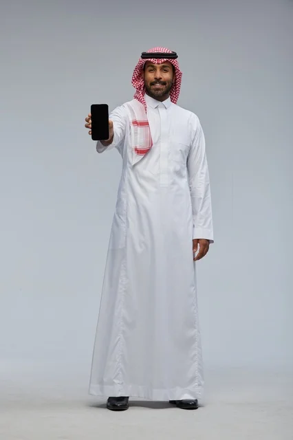 رجل سعودي يرتدي الثوب التقليدي ممسكاً بهاتف ذكي