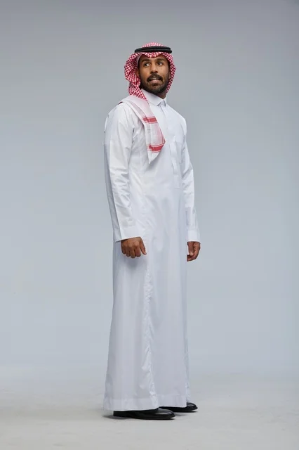 رجل سعودي بالزي التقليدي أمام خلفية رمادية