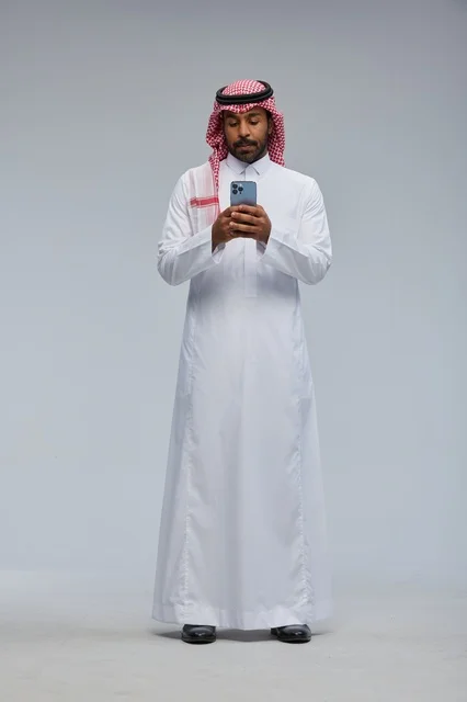 رجل سعودي بالزي التقليدي يستخدم الهاتف الذكي