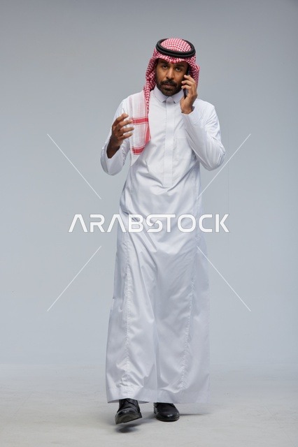 رجل سعودي بالثوب التقليدي يتحدث عبر الهاتف الذكي