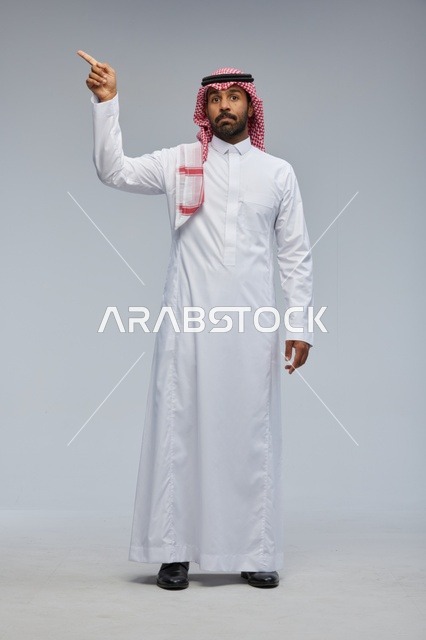 Saudi Man in Traditional Thobe Pointing Up in Studio