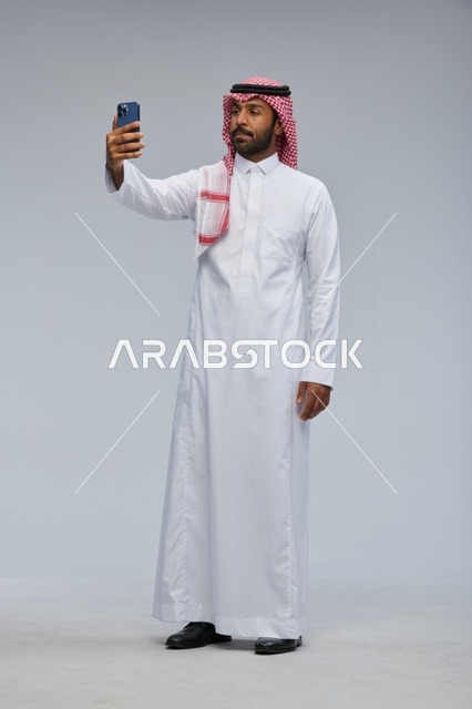 رجل سعودي بالثوب التقليدي يلتقط صورة سيلفي بالجوال