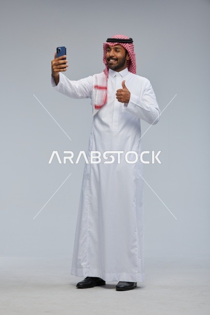 رجل سعودي يلتقط سيلفي بالهاتف مع إيماءة الإبهام
