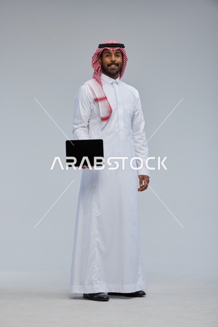 رجل سعودي يحمل جهازاً لوحياً بملابس تقليدية