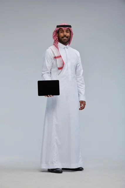 رجل سعودي يحمل جهازاً لوحياً بملابس تقليدية
