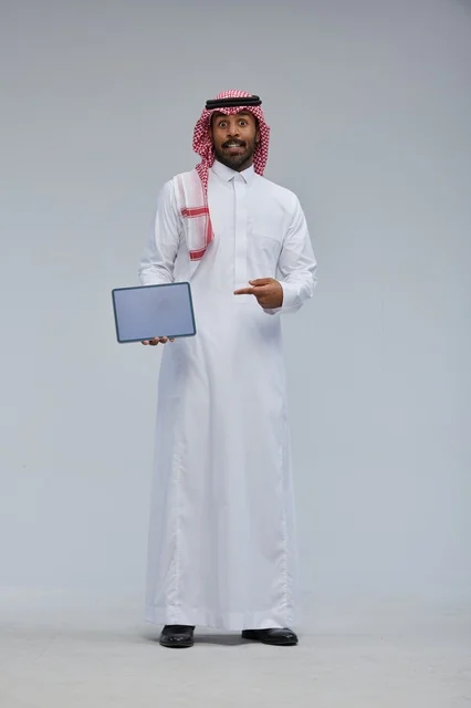 رجل سعودي بالثوب التقليدي يشير إلى جهاز لوحي في الاستوديو