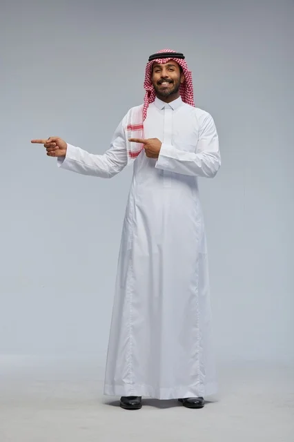 رجل سعودي بالزي التقليدي يشير على خلفية رمادية