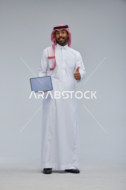 رجل سعودي يحمل جهاز لوحي مع إشارة الإبهام