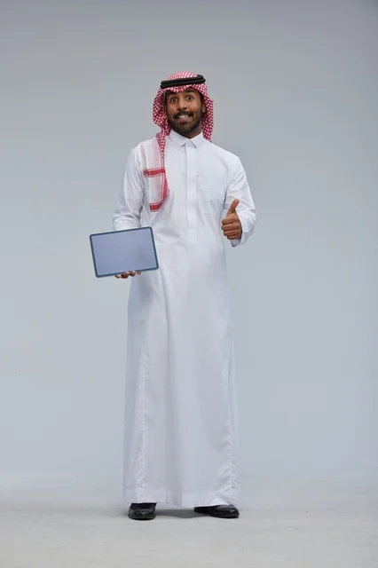رجل سعودي يحمل جهاز لوحي مع إشارة الإبهام