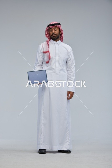 رجل سعودي يحمل جهازاً لوحياً في الاستوديو