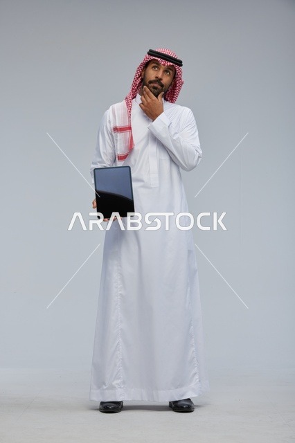 رجل سعودي يحمل جهازاً لوحياً في وضعية تفكير