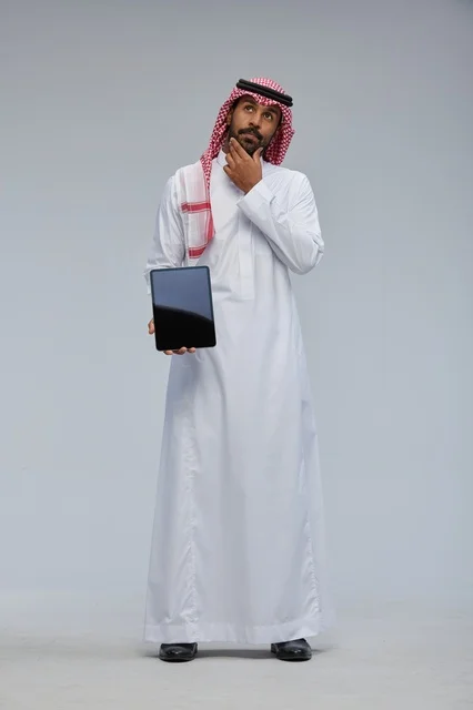 رجل سعودي يحمل جهازاً لوحياً في وضعية تفكير