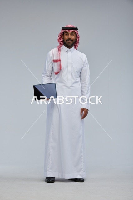 رجل سعودي بالزي التقليدي يمسك جهازاً لوحياً
