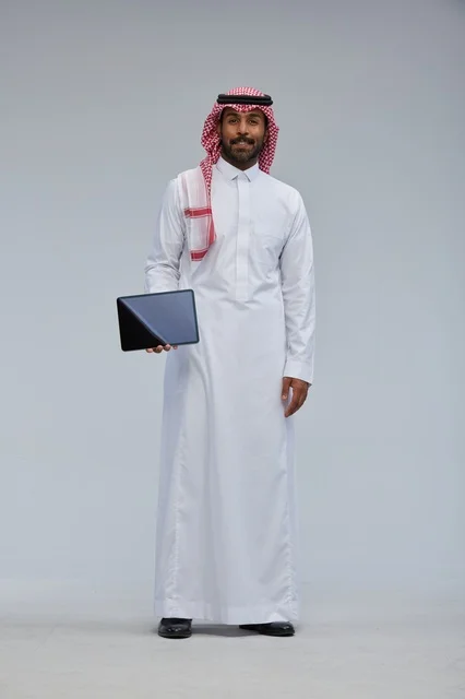 رجل سعودي بالزي التقليدي يمسك جهازاً لوحياً