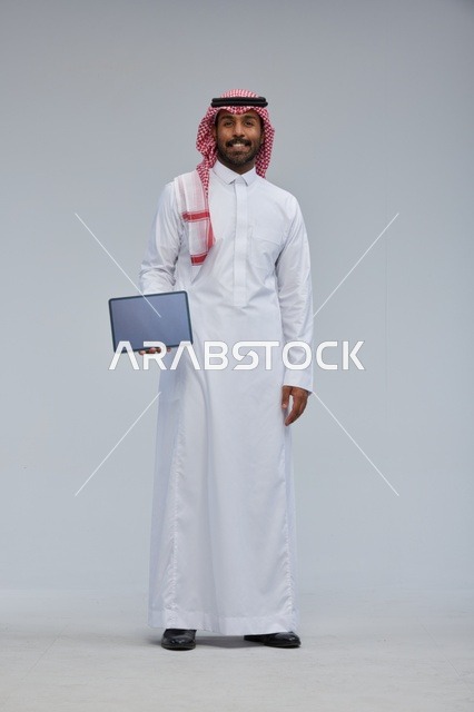 رجل سعودي بالثوب والشماغ يحمل جهازاً لوحياً ذكياً