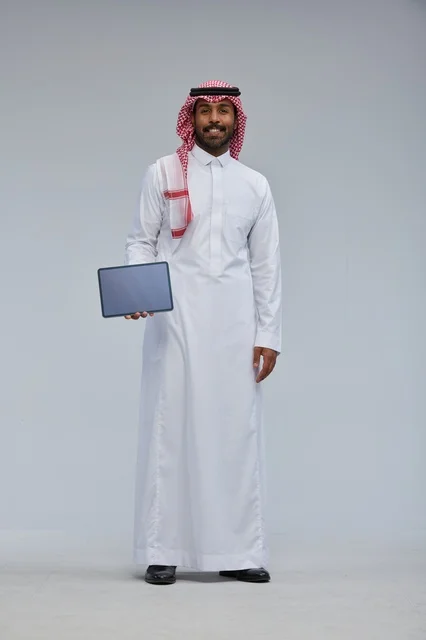 رجل سعودي بالثوب والشماغ يحمل جهازاً لوحياً ذكياً