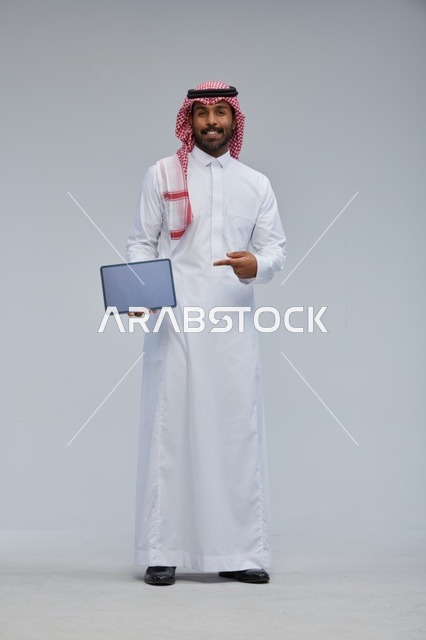 رجل سعودي يحمل جهازًا لوحيًا بالزي التقليدي