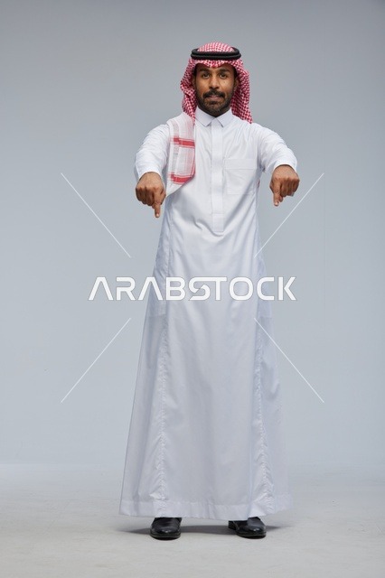 رجل سعودي بالزي التقليدي يشير إلى الأسفل