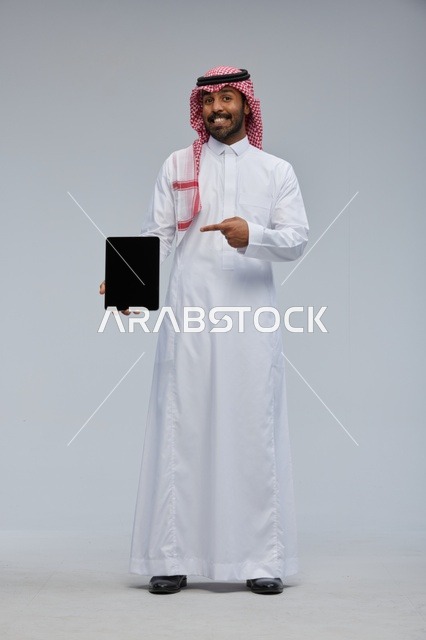 رجل سعودي يحمل جهازاً لوحياً بالزي التقليدي