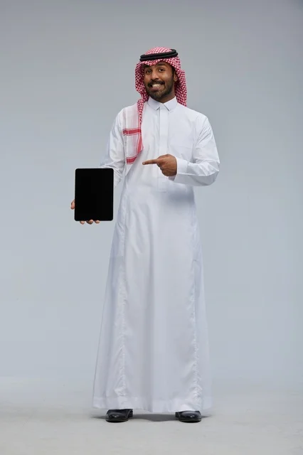 رجل سعودي يحمل جهازاً لوحياً بالزي التقليدي