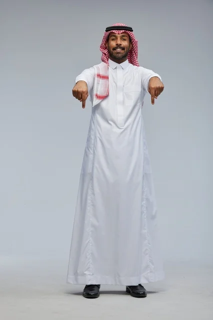 رجل سعودي بالزي التقليدي يشير للأسفل في استوديو