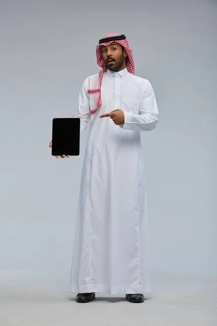 رجل سعودي يحمل جهاز لوحي بشاشة فارغة في استوديو