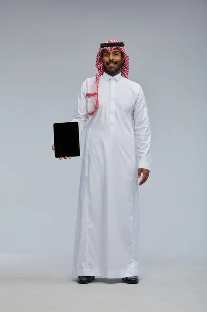 رجل سعودي يحمل جهاز لوحي على خلفية رمادية