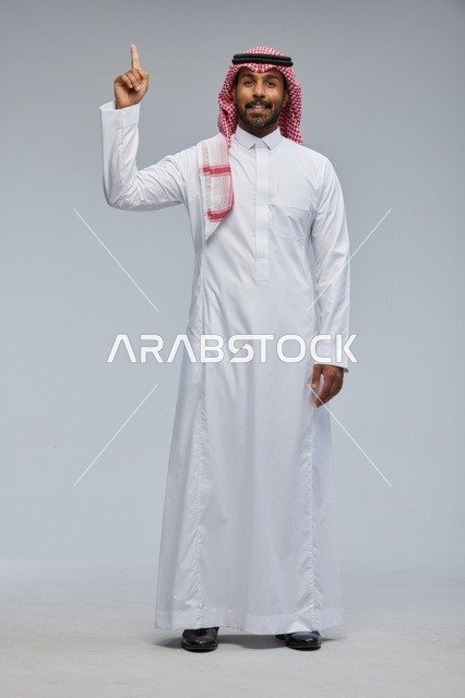 Saudi Man in Traditional Thobe Pointing Up in Studio