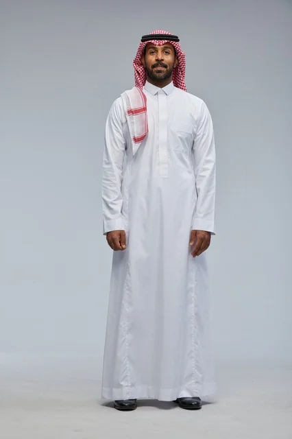 رجل سعودي بالزي التقليدي أمام خلفية رمادية