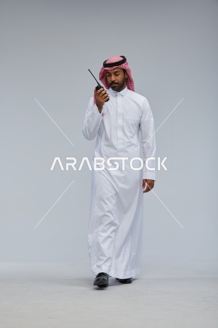 Saudi Man Using Walkie Talkie on Gray Background