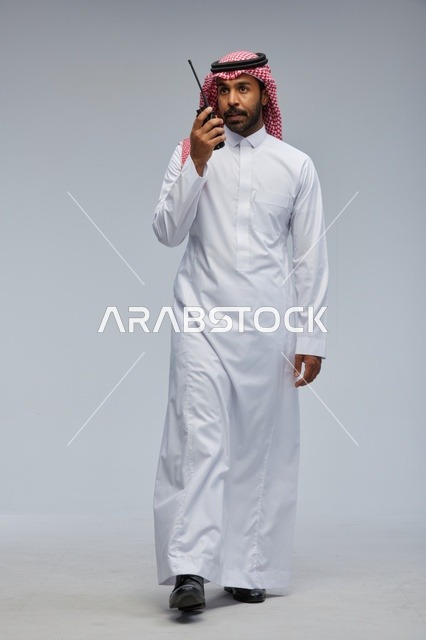 Saudi Man Using Handheld Walkie Talkie on Grey Background