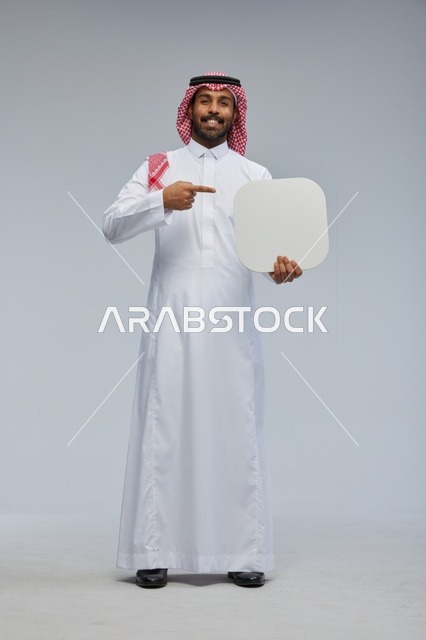 رجل سعودي مبتسم بالزي التقليدي يحمل لوحة بيضاء فارغة