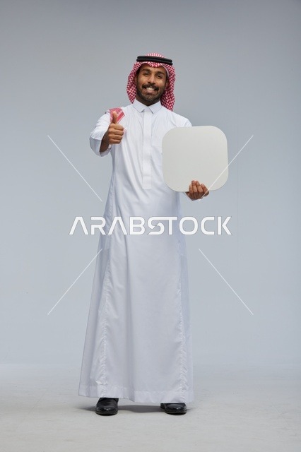 رجل سعودي مبتسم يحمل لوحة بيضاء فارغة بخلفية رمادية