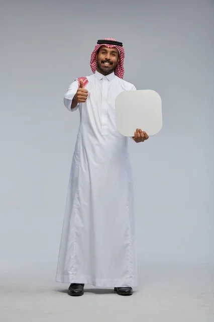 رجل سعودي مبتسم يحمل لوحة بيضاء فارغة بخلفية رمادية