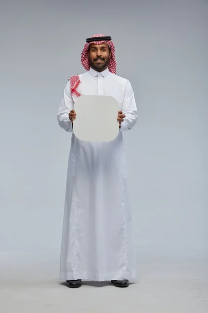 رجل سعودي مبتسم يحمل لوحة بيضاء فارغة في الاستوديو