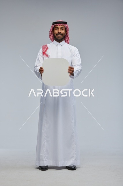 رجل سعودي مبتسم يحمل لوحة بيضاء فارغة في الاستوديو